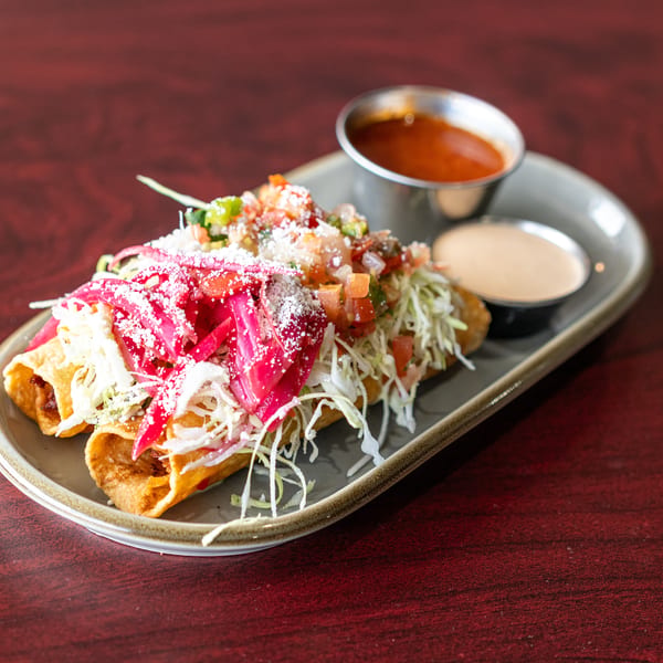 Three taquitos topped with shredded cabbage, pickled red onions, pico de gallo, and cotija cheese.