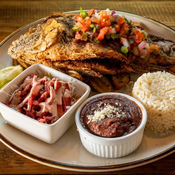 Whole fried fish topped with salsa, served with rice, beans, coleslaw, and a lime wedge.