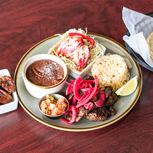 A colorful platter with grilled meat, rice, beans, salad, pico de gallo, and fried plantains.