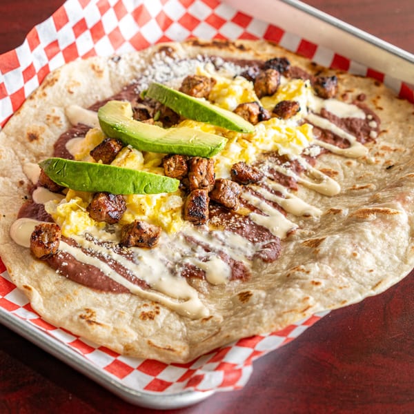 Breakfast burrito with scrambled eggs, sausage, avocado, and sauce on a red checkered liner.